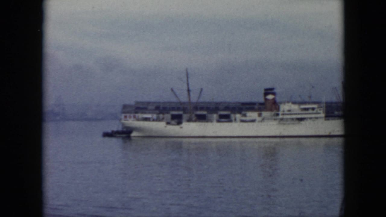 1956 Cuba 8mm frame showing a large white cargo ship across calm harbor water, with cranes and a dark-edged film border.