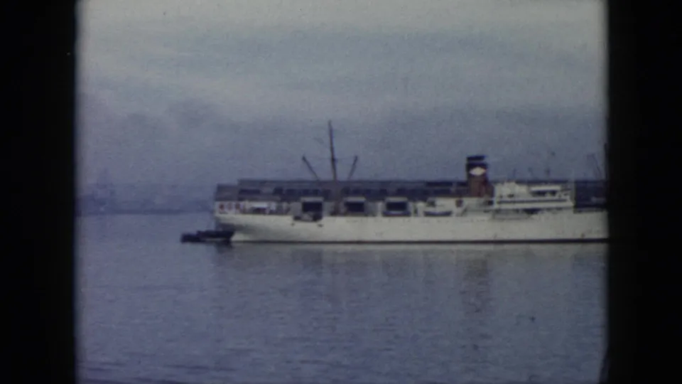 1956 Cuba 8mm frame showing a large white cargo ship across calm harbor water, with cranes and a dark-edged film border.