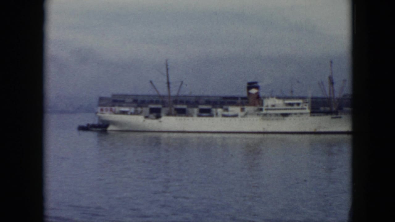 1956 Cuba harbor view of a white cargo ship filmed from a distance, with deck cranes and soft 8mm color grain.