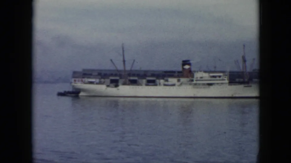 1956 Cuba harbor view of a white cargo ship filmed from a distance, with deck cranes and soft 8mm color grain.