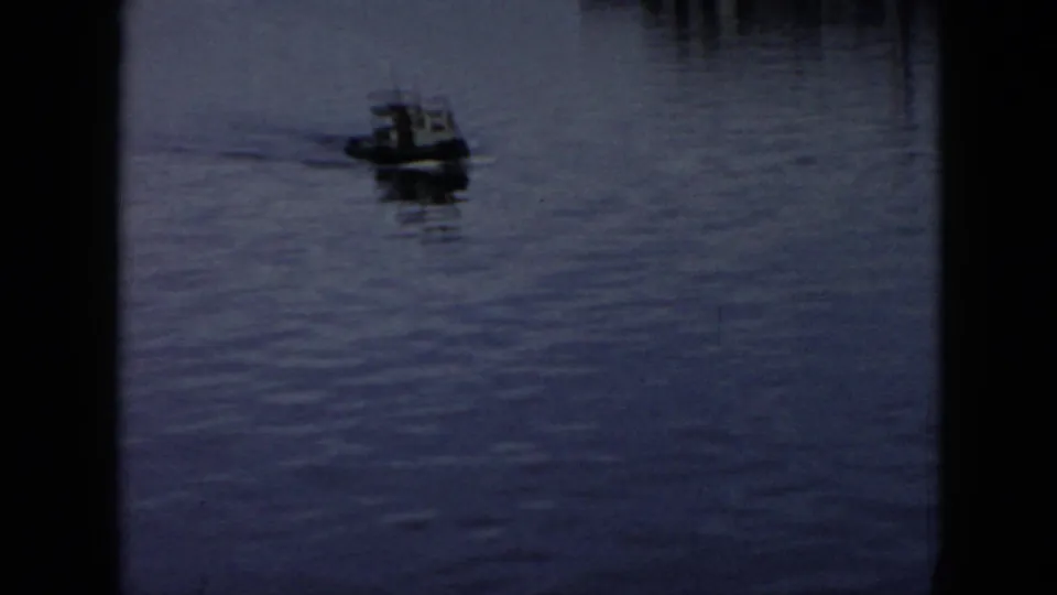 1956 Cuba 8mm frame with a small motorized boat crossing the river, its wake trailing across muted blue water.
