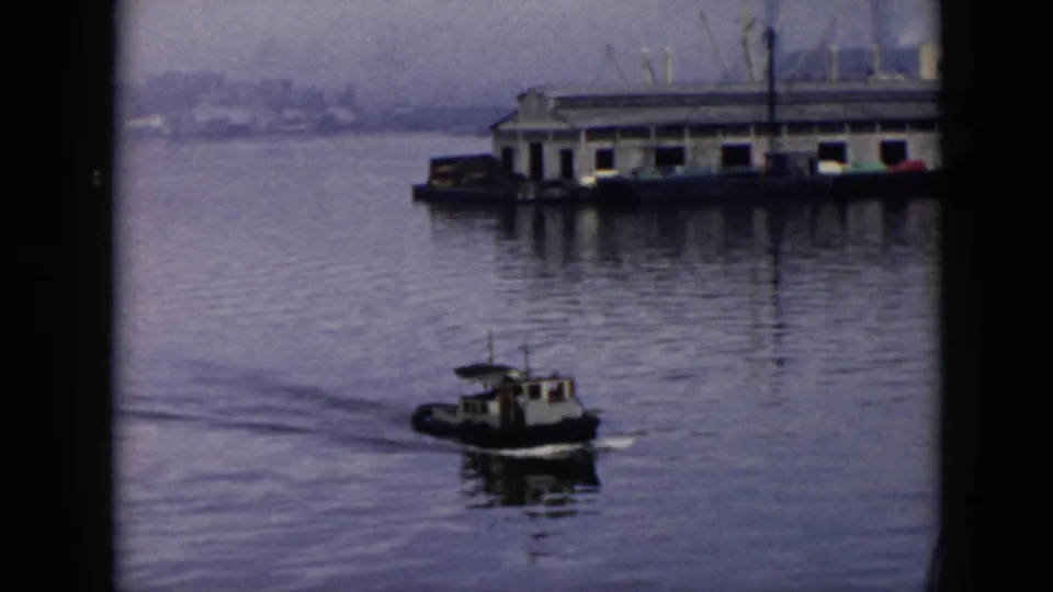 The tugboat continues through calm Cuban harbor water, passing a long dock structure with industrial forms in the background.