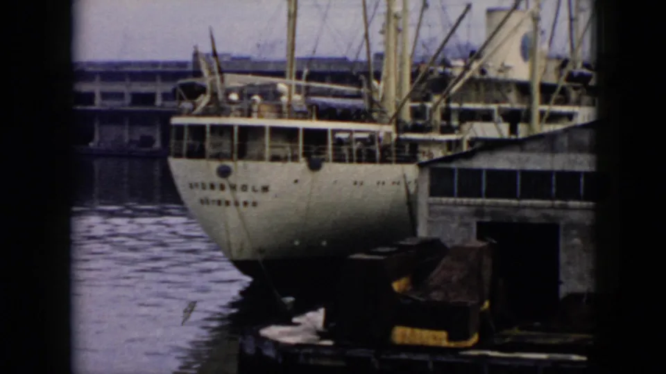 A larger vessel is moored at a Cuban dock, with painted stern lettering, rigging, pilings, and harbor water visible.