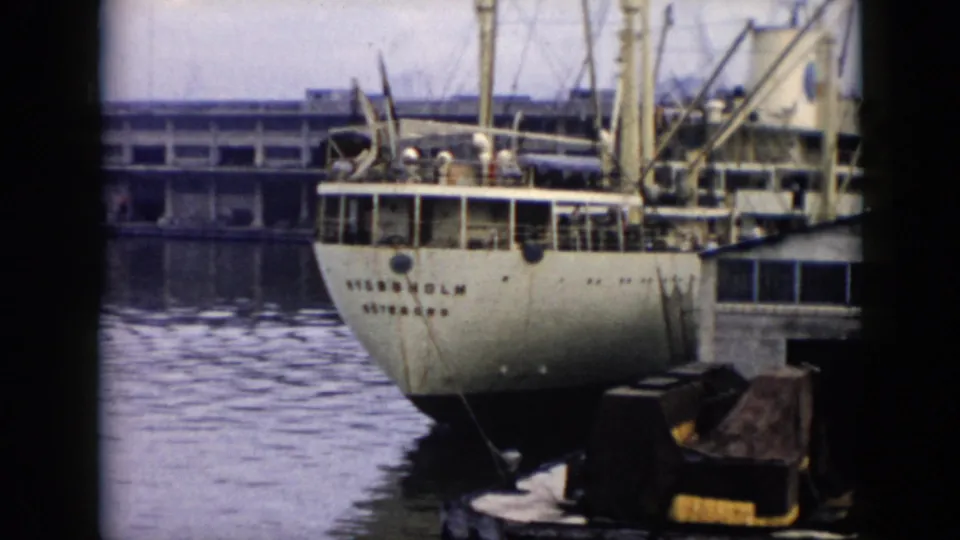 The docked vessel remains framed near the waterfront in 1956 Cuba, showing rigging, stern markings, pilings, and reflective harbor water.
