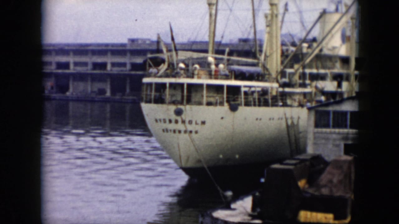 1956 Cuba 8mm frame showing the stern of a white vessel marked STOCKHOLM at a dock, with deck figures, pier structure, mooring lines, and harbor water visible.
