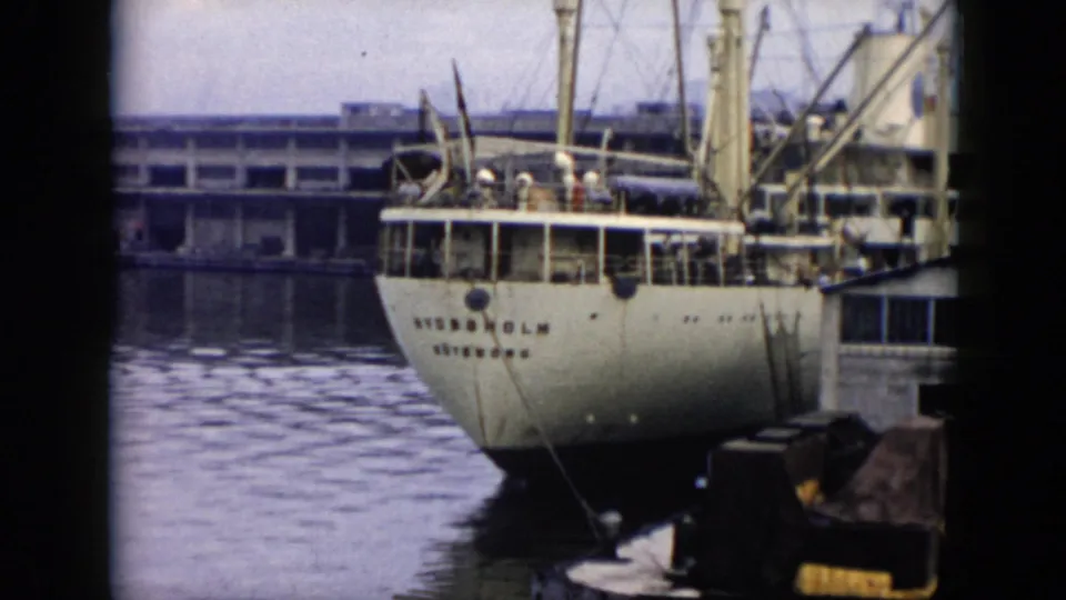 1956 Cuba 8mm frame showing the stern of a white vessel marked STOCKHOLM at a dock, with deck figures, pier structure, mooring lines, and harbor water visible.