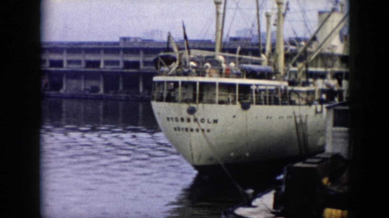1956 Cuba 8mm frame of the ship STOCKHOLM at a waterfront dock, with people on deck, a long pier in the background, and calm water below.