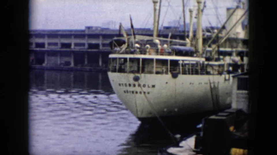 1956 Cuba 8mm frame of the ship STOCKHOLM at a waterfront dock, with people on deck, a long pier in the background, and calm water below.