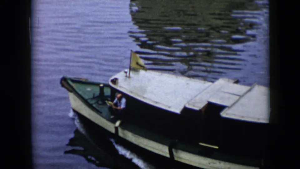 1956 Cuba 8mm frame of a small harbor motorboat passing through rippled water, with a man at the controls, a yellow flag, and reflections on the surface.