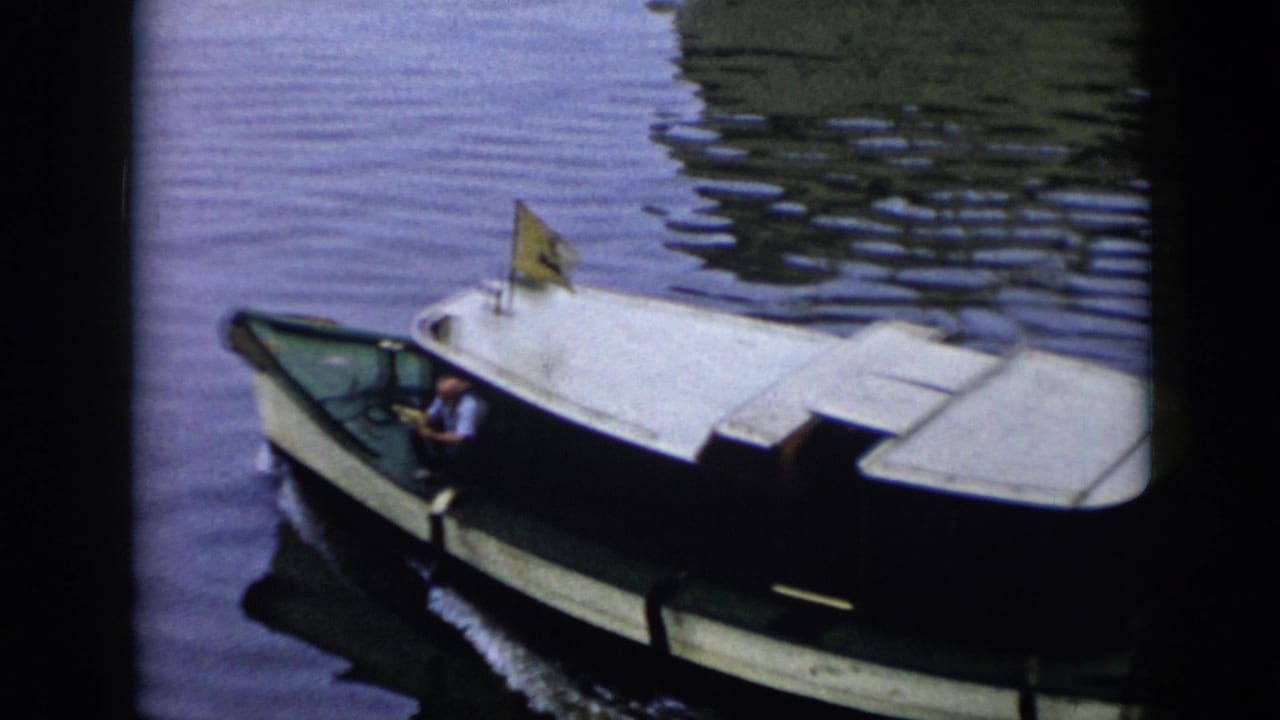 1956 Cuba 8mm frame showing a green-hulled cabin motorboat with a man steering and a small yellow flag on calm water.