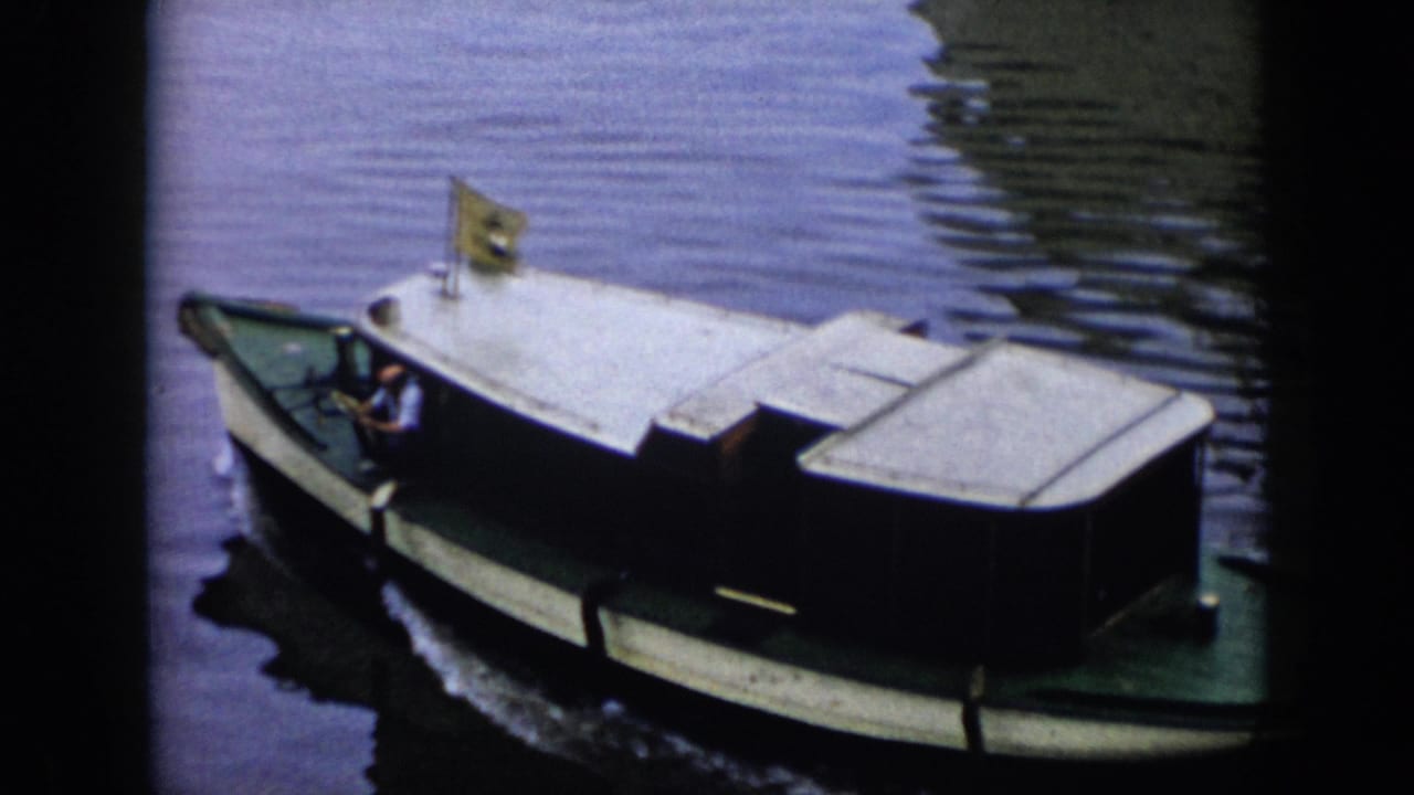 1956 Cuba home-movie frame of a white-roofed motorboat moving on reflective water as a man sits near the front controls.
