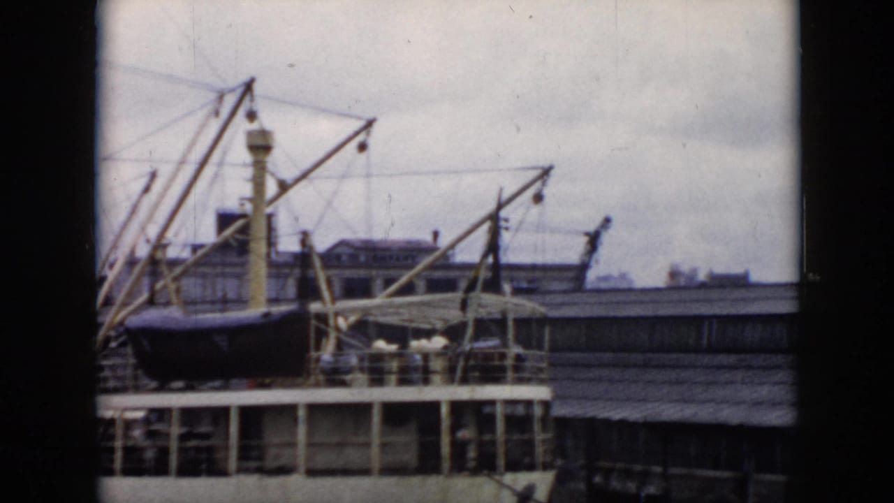 1956 Cuba home-movie frame showing a docked passenger ship with a dark lifeboat, pale cranes, deck railings, and overcast sky.