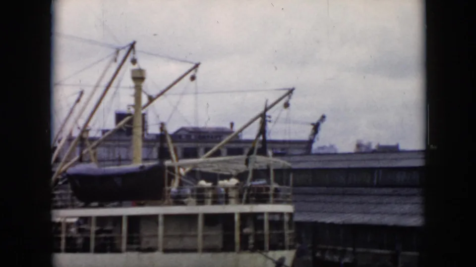 1956 Cuba home-movie frame showing a docked passenger ship with a dark lifeboat, pale cranes, deck railings, and overcast sky.