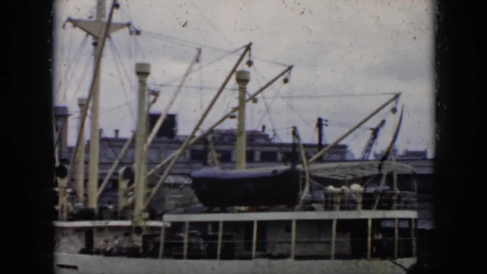1956 Cuba home-movie view of a passenger ship at port, with the lifeboat centered among masts, cranes, and pier structure.
