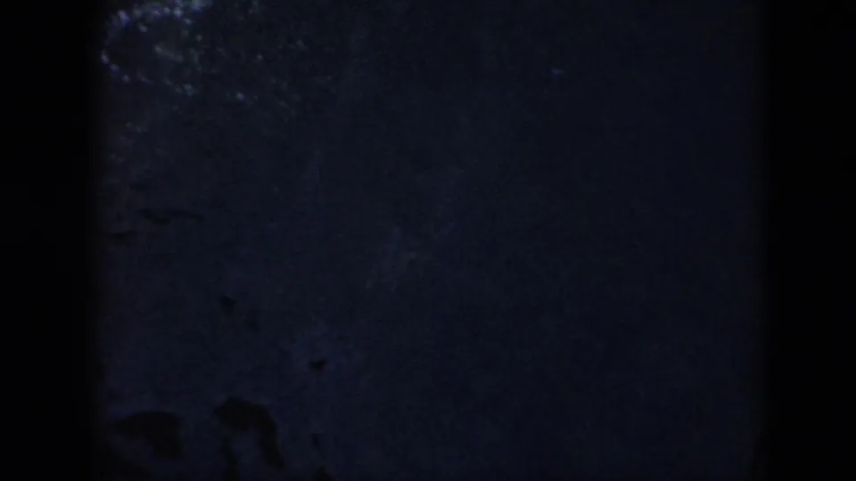 The swimmer has dropped from view, leaving dark pool water, faint ripples, and 8mm frame shadows.