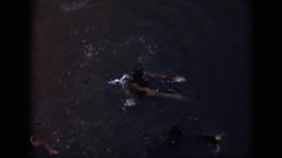 1956 Cuba 8mm frame showing two swimmer silhouettes in dark water, with one figure reaching across the surface.