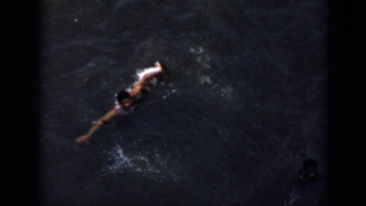 High-angle 1956 Cuba 8mm frame showing a swimmer in dark water, partly softened by grain and low exposure.