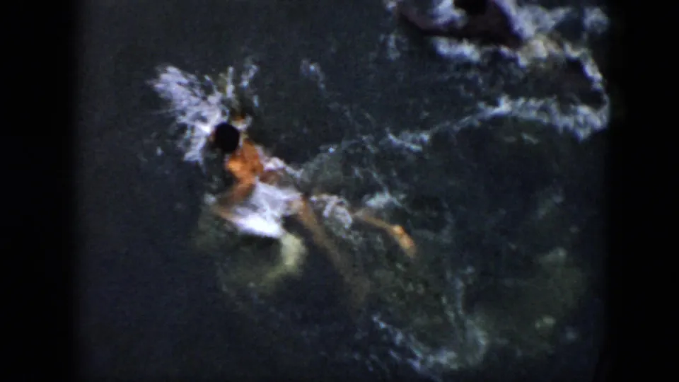 High-angle 1956 Cuba home-movie frame showing a swimmer creating white splashes in dark ocean water.