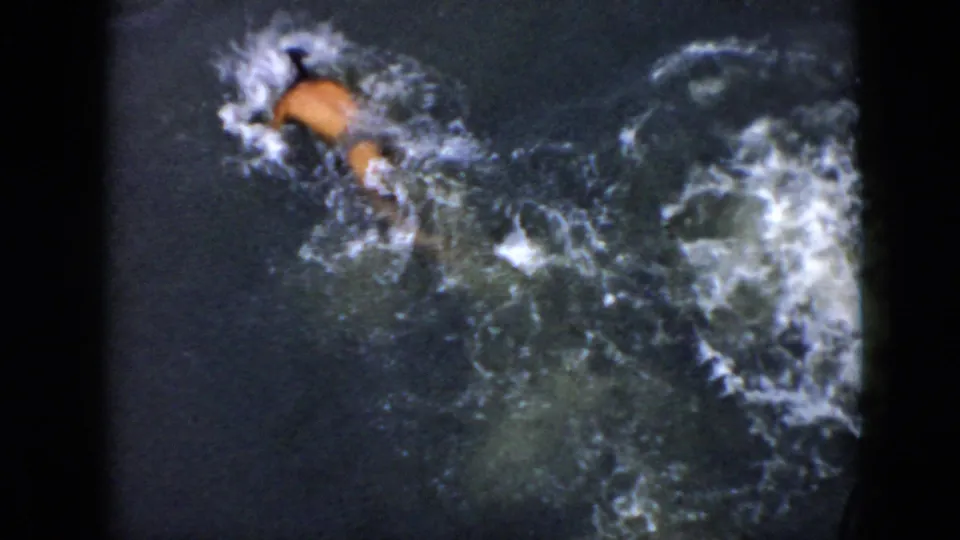 Grainy 1956 Cuba 8mm frame with a swimmer partly obscured by foam and splashing dark water.