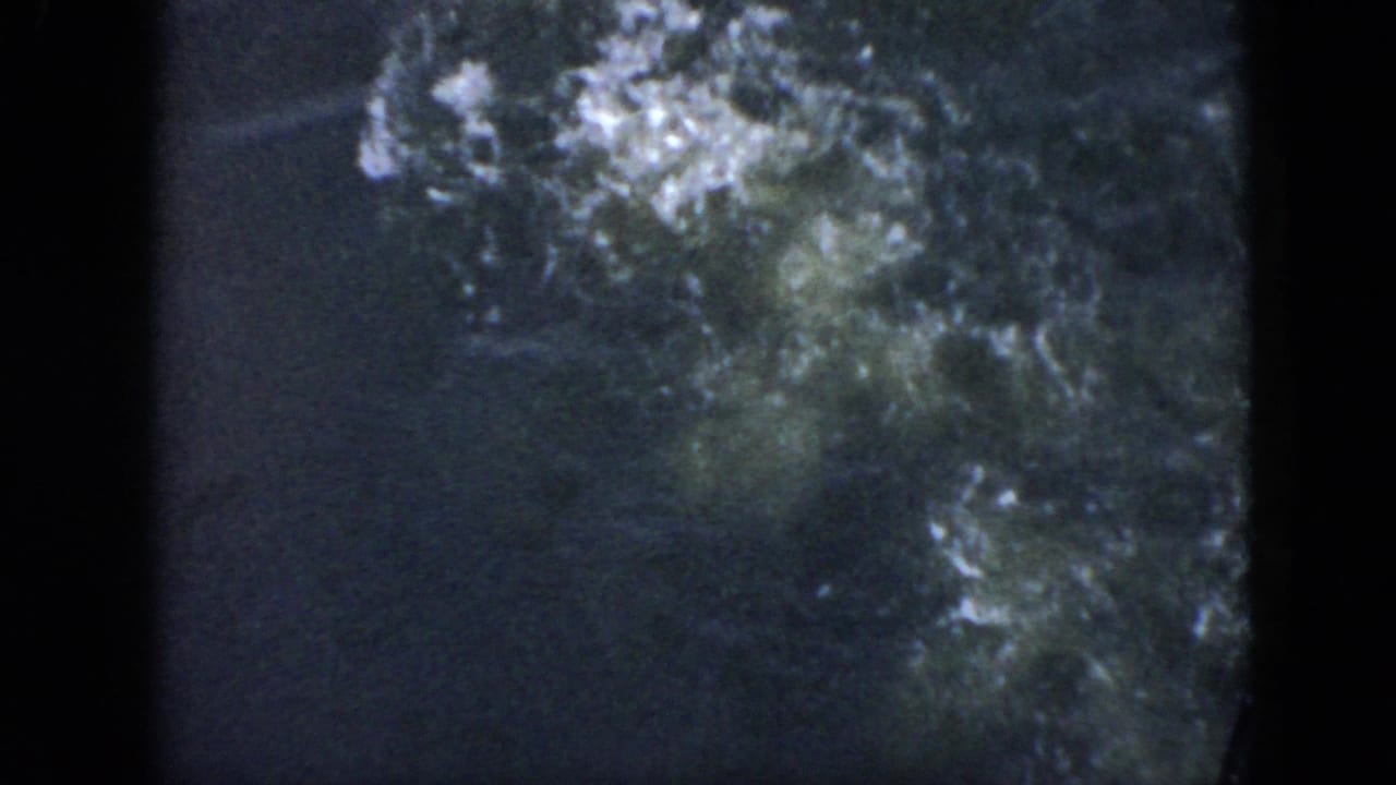 1956 Cuba 8mm frame showing dark water with white bubbles spreading after a swimmer dives below the surface.