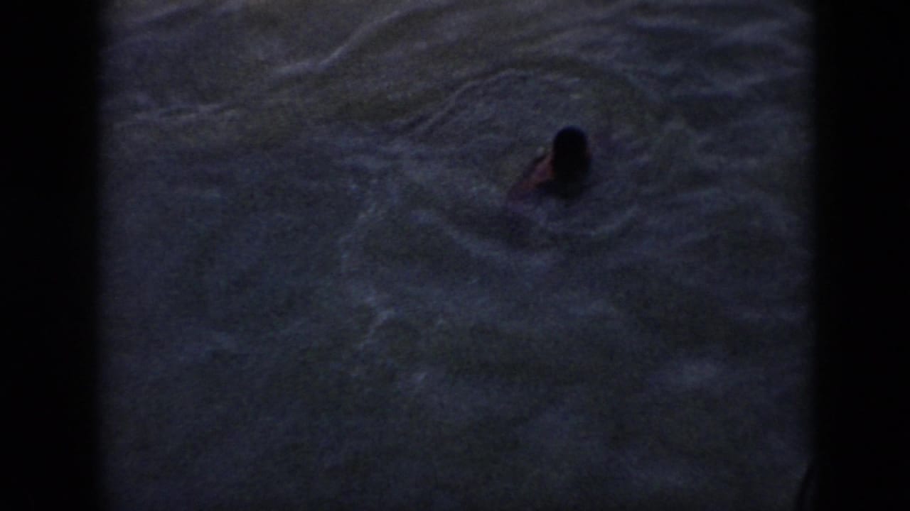 1956 Cuba 8mm frame showing a person swimming in dark water below a boat railing.