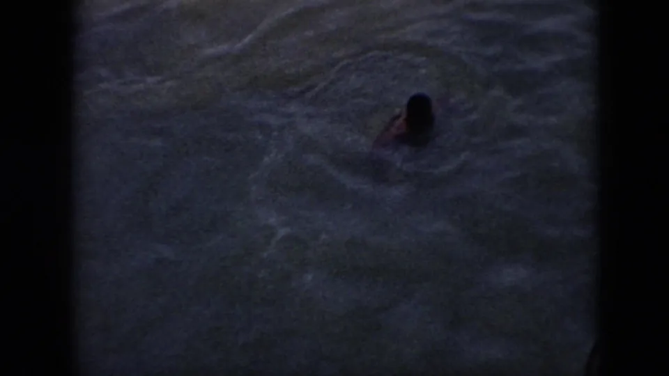 1956 Cuba 8mm frame showing a person swimming in dark water below a boat railing.
