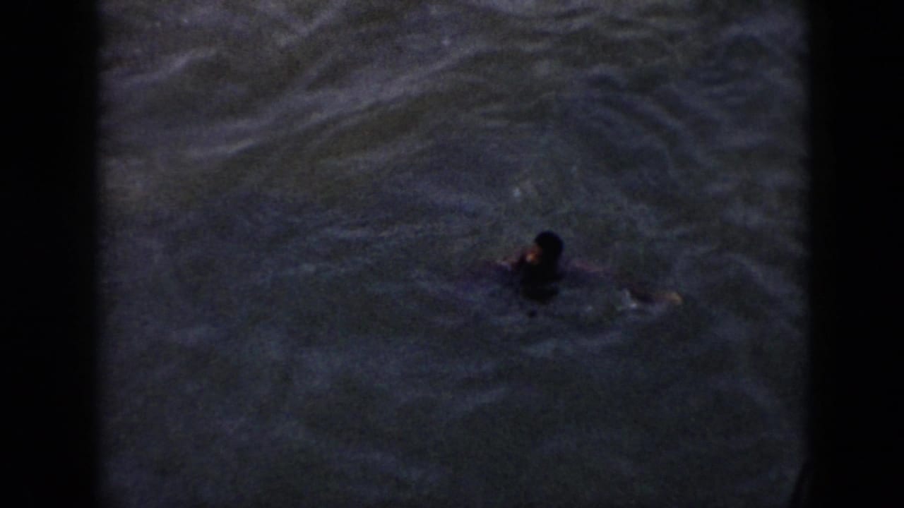 A person swims in rippled water beside a boat in 1956 Cuba home-movie footage.