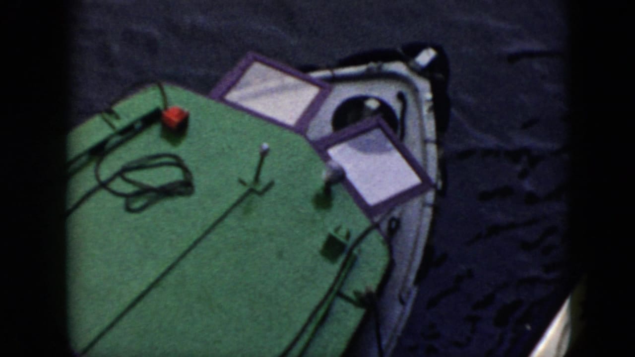 1956 Cuba home-movie frame showing the bow area of a small boat with a green deck, rope, and dark water around it.