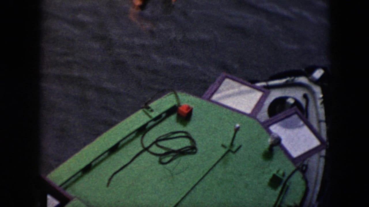 Green-decked boat at right with rope and railing on dark water.