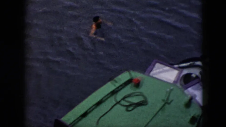 A man swims in dark water above the small green-decked boat, visible in this high-angle 1956 Cuba home-movie frame.