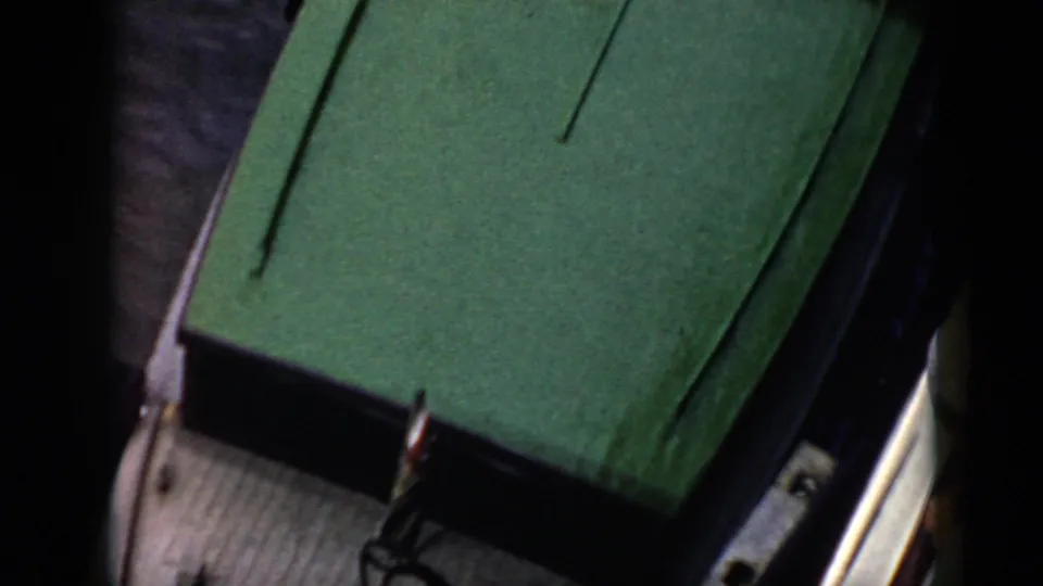 The frame shows a closer view of the green boat deck with deck hardware and a sliver of water along the edge.