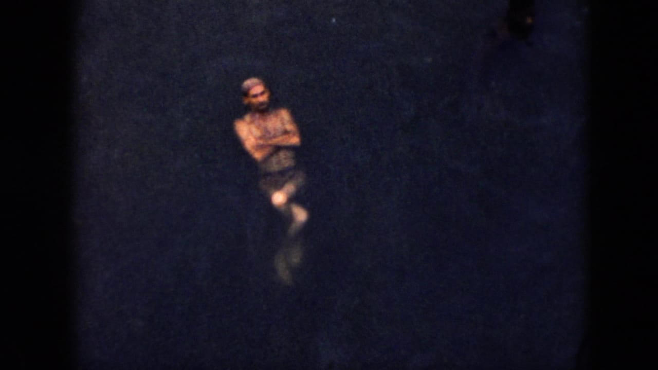 1956 Cuba home-movie frame with an adult male swimmer floating upright in dark lake water.