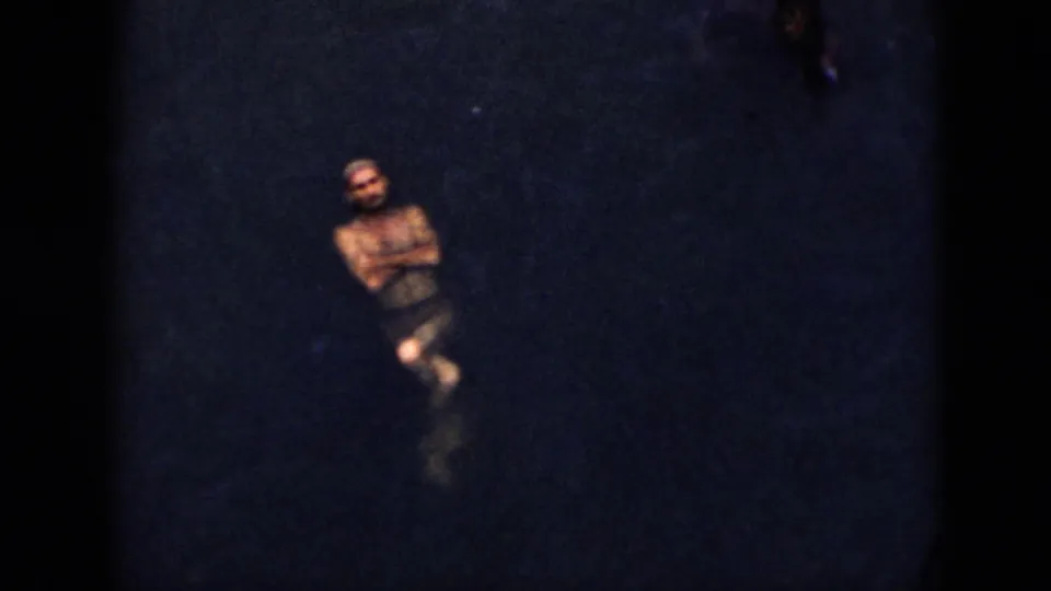 1956 Cuba 8mm frame showing an adult man floating near the surface of a dark lake.