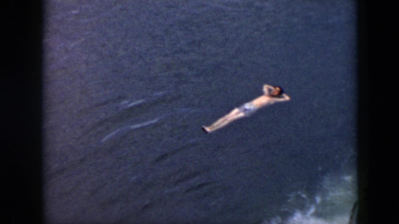 1956 Cuba 8mm frame showing a man in light swim trunks floating on his back in dark blue water.