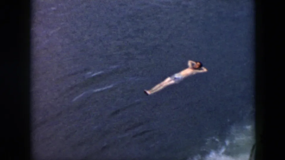 1956 Cuba 8mm frame showing a man in light swim trunks floating on his back in dark blue water.