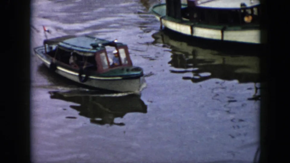 1956 Cuba 8mm frame showing a small motorboat with passengers crossing calm water near a larger vessel.