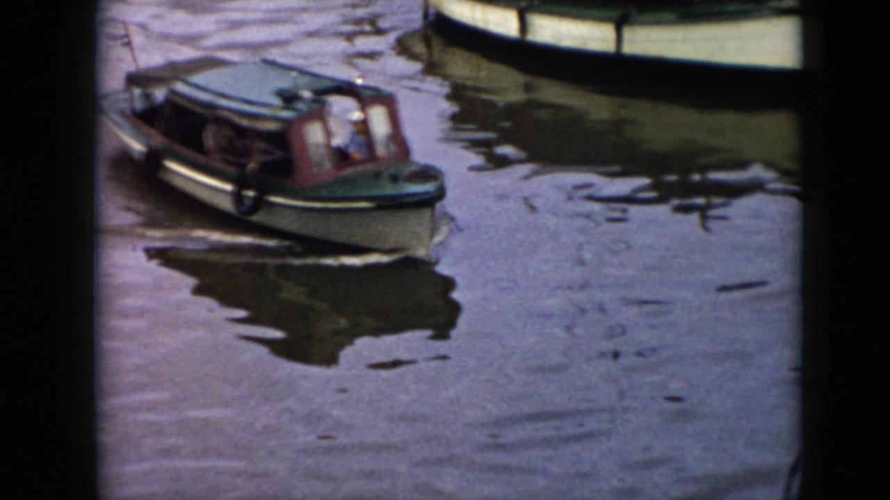 1956 Cuba home-movie frame showing a green cabin motorboat crossing calm dark water, with another boat cropped at the top edge.