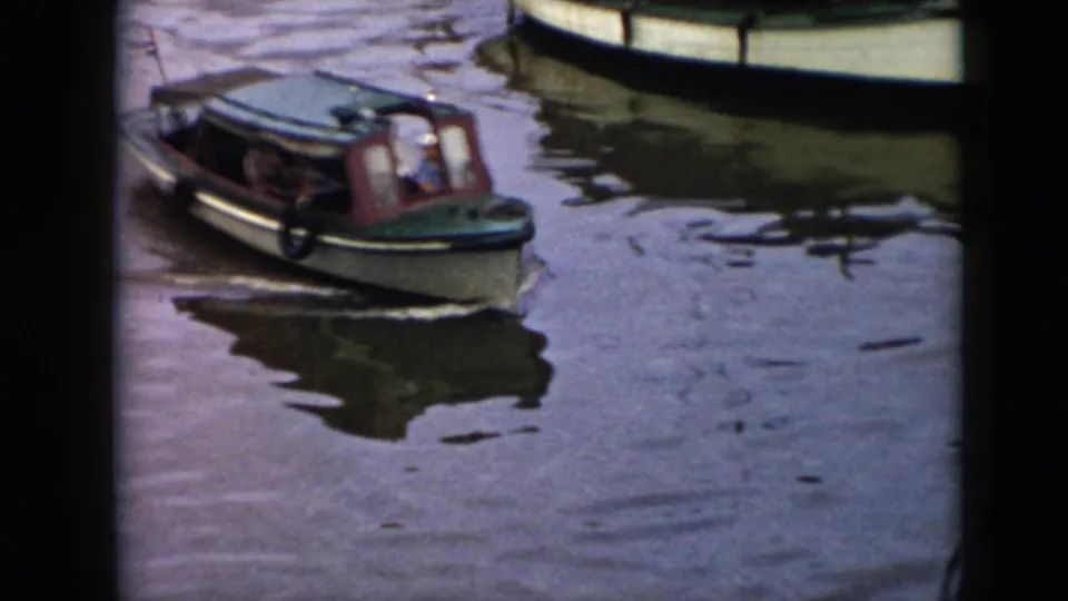 1956 Cuba home-movie frame showing a green cabin motorboat crossing calm dark water, with another boat cropped at the top edge.