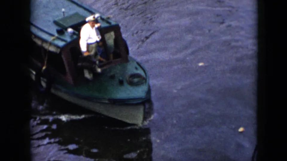 1956 Cuba frame showing an adult man in a white sailor-style uniform standing on a green cabin motorboat on calm water.