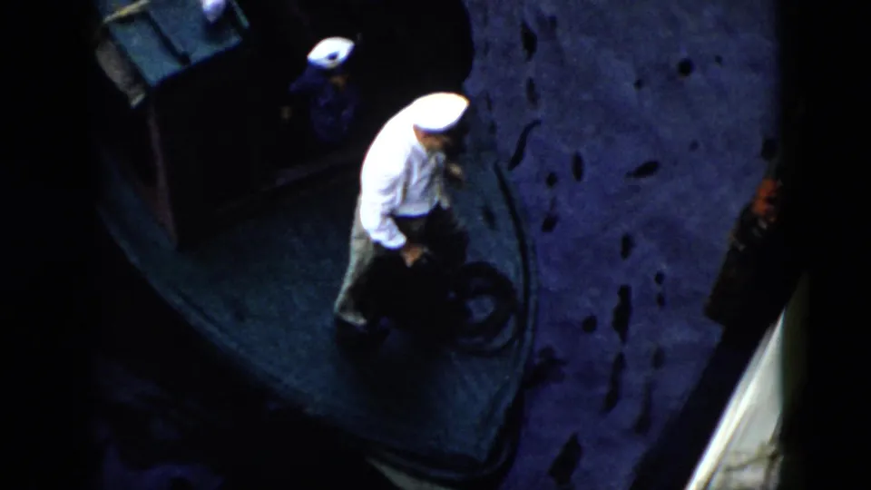 1956 Cuba home-movie frame showing a uniformed man near a coiled rope on a small boat, with another crew member in blue nearby.