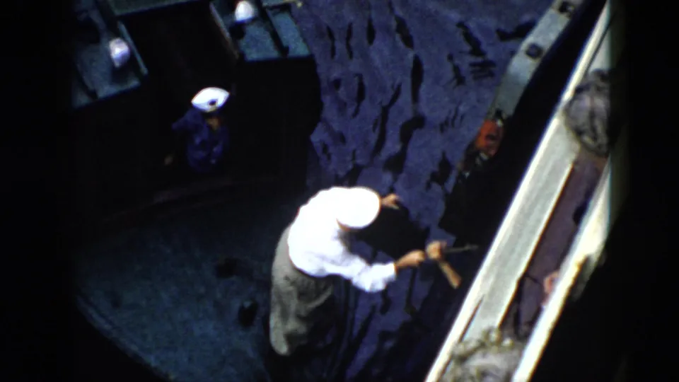 1956 Cuba home-movie frame of a white-capped man leaning toward the side of another vessel or dock while another person stands on the boat.