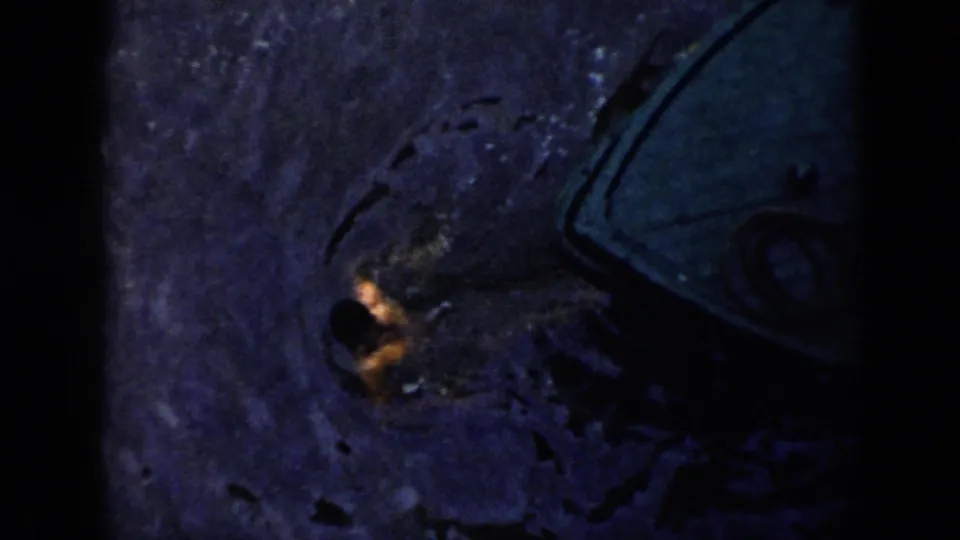 1956 Cuba night footage frame with a person partly surfaced in dark water near the curved outline of a boat.