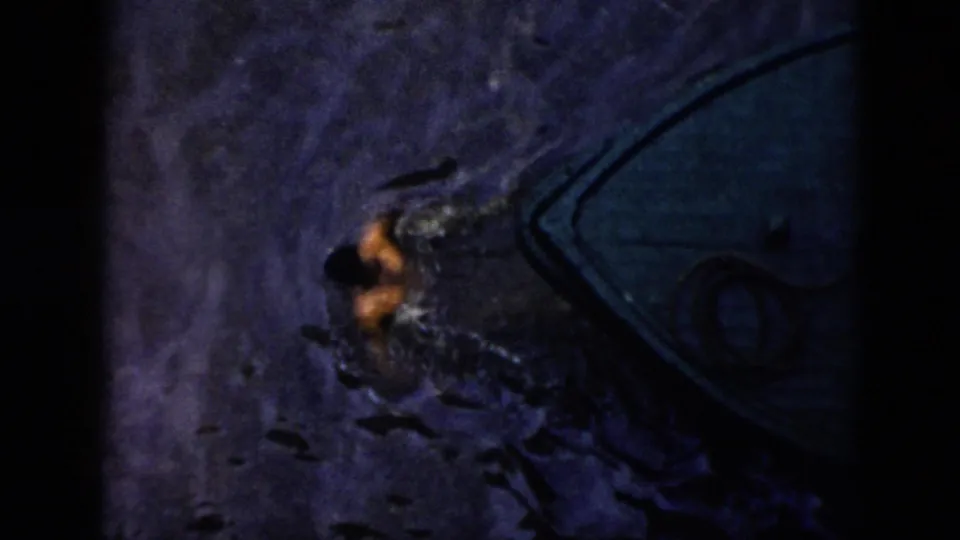 1956 Cuba 8mm frame showing a person moving through choppy, dark water beside a boat at night.