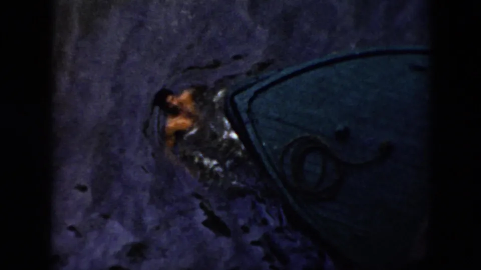1956 Cuba home-movie frame of a person in disturbed dark water next to a boat outline under harsh night light.