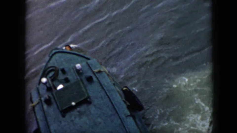 1956 Cuba 8mm frame with the boat bow viewed from above, deck gear visible, and wake spreading across gray-green water.