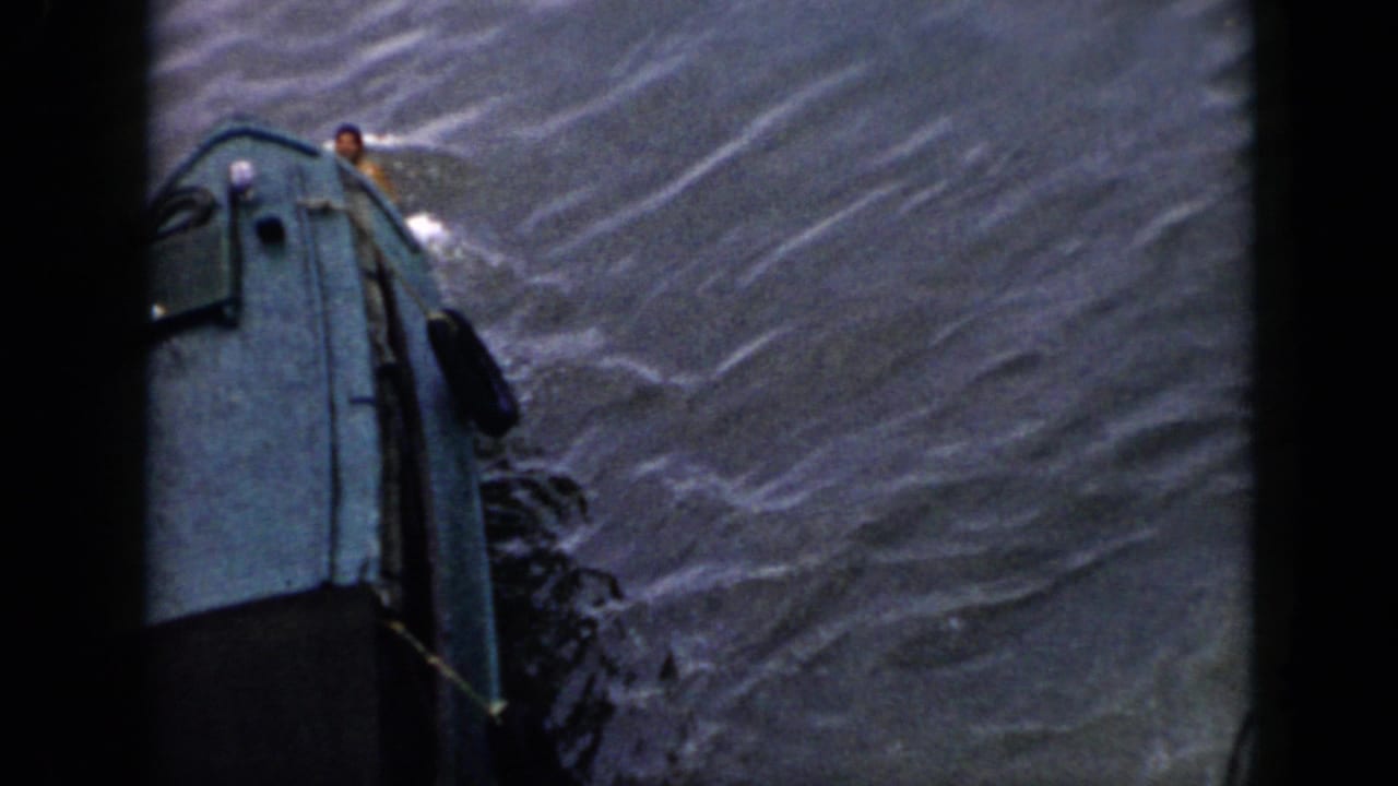 1956 Cuba home-movie frame with a weathered green boat moving through water and a swimmer near the bow.