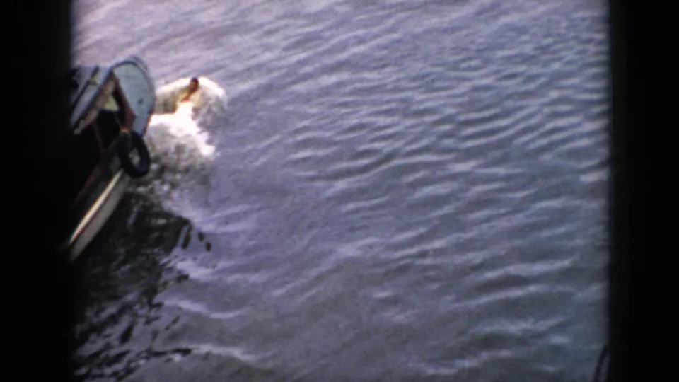 1956 Cuba home-movie frame with a swimmer raising an arm beside a small boat on choppy water.