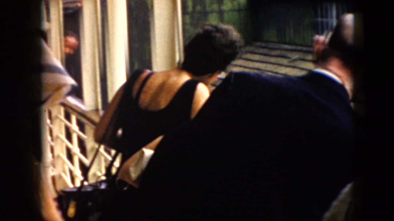 Adults in 1956 Cuba appear on a covered veranda, leaning over the railing while watching something below.