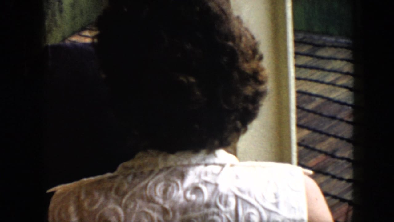 1956 Cuba home-movie frame showing a woman in a light patterned dress from behind near a dock or balcony edge.