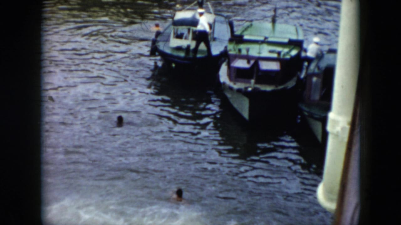 1956 Cuba home-movie frame showing small boats, swimmers, and docked harbor vessels seen from above.